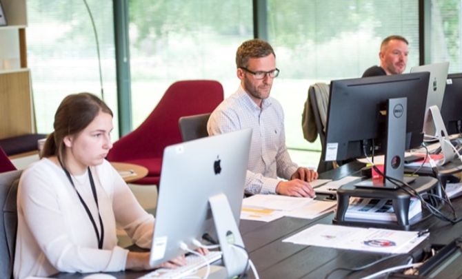 Three professionals collaborating on computers in an office, highlighting the shift to online faxing software in business communication.